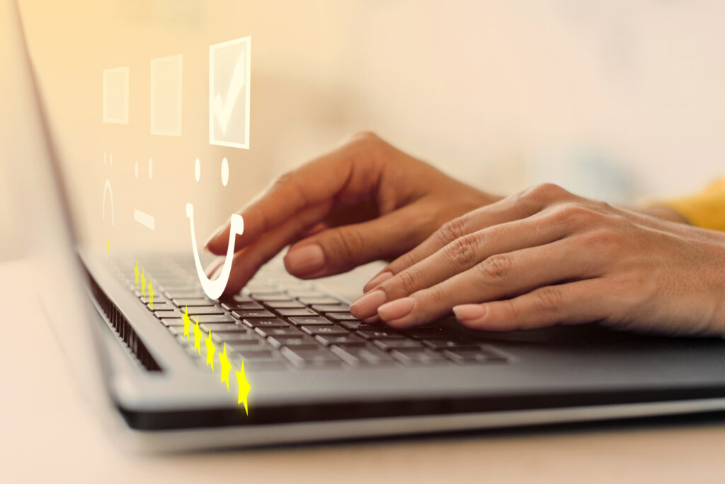 Nahaufnahme von Händen, die auf einer Laptop-Tastatur tippen, mit grafischen Symbolen von Smileys und Sternen darüber liegend, die auf ein Bewertungssystem hinweisen. Marke anmelden.